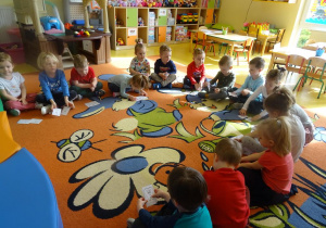 Dzieci siedzą w kręgu na dywanie, przed sobą na dywanie mają rozłożone dwie sylwety zębów smutną i wesołą.
